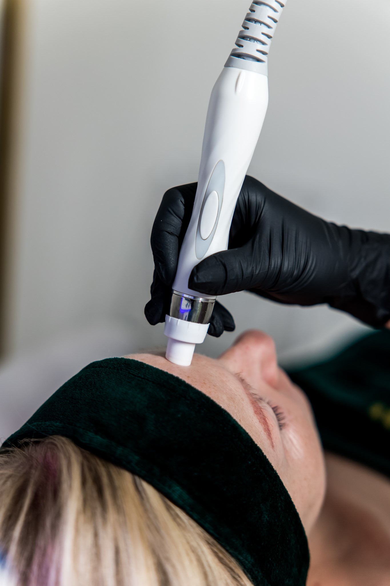 Zabieg oczyszczania i pielęgnacji skóry twarzy wykonywany urządzeniem kosmetycznym, klientka w opasce relaksacyjnej