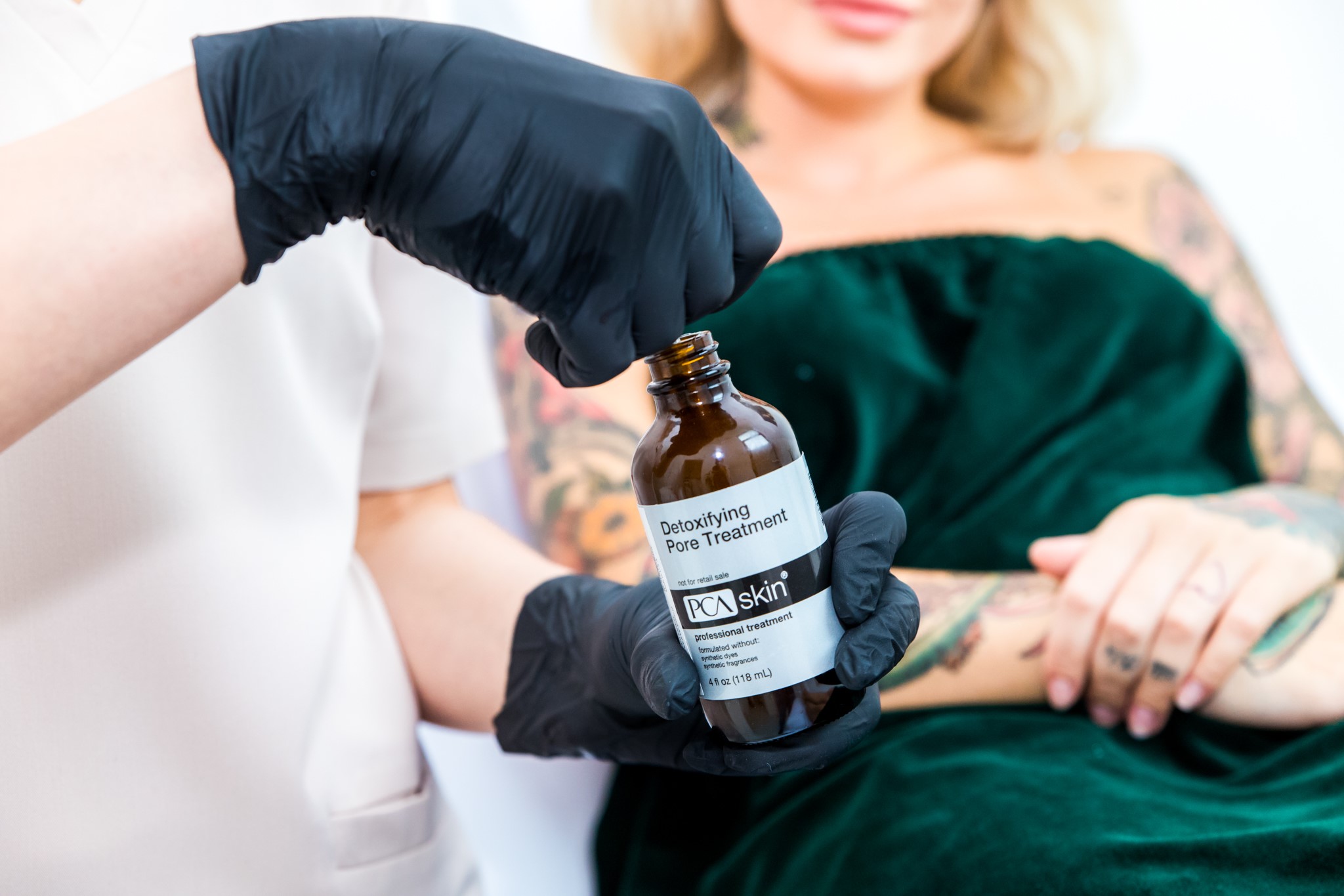 Specjalistka trzymająca profesjonalny preparat do oczyszczania skóry podczas zabiegu pielęgnacyjnego w gabinecie beauty. Preparat PCA skin - Detoxifying Pore Treatment.