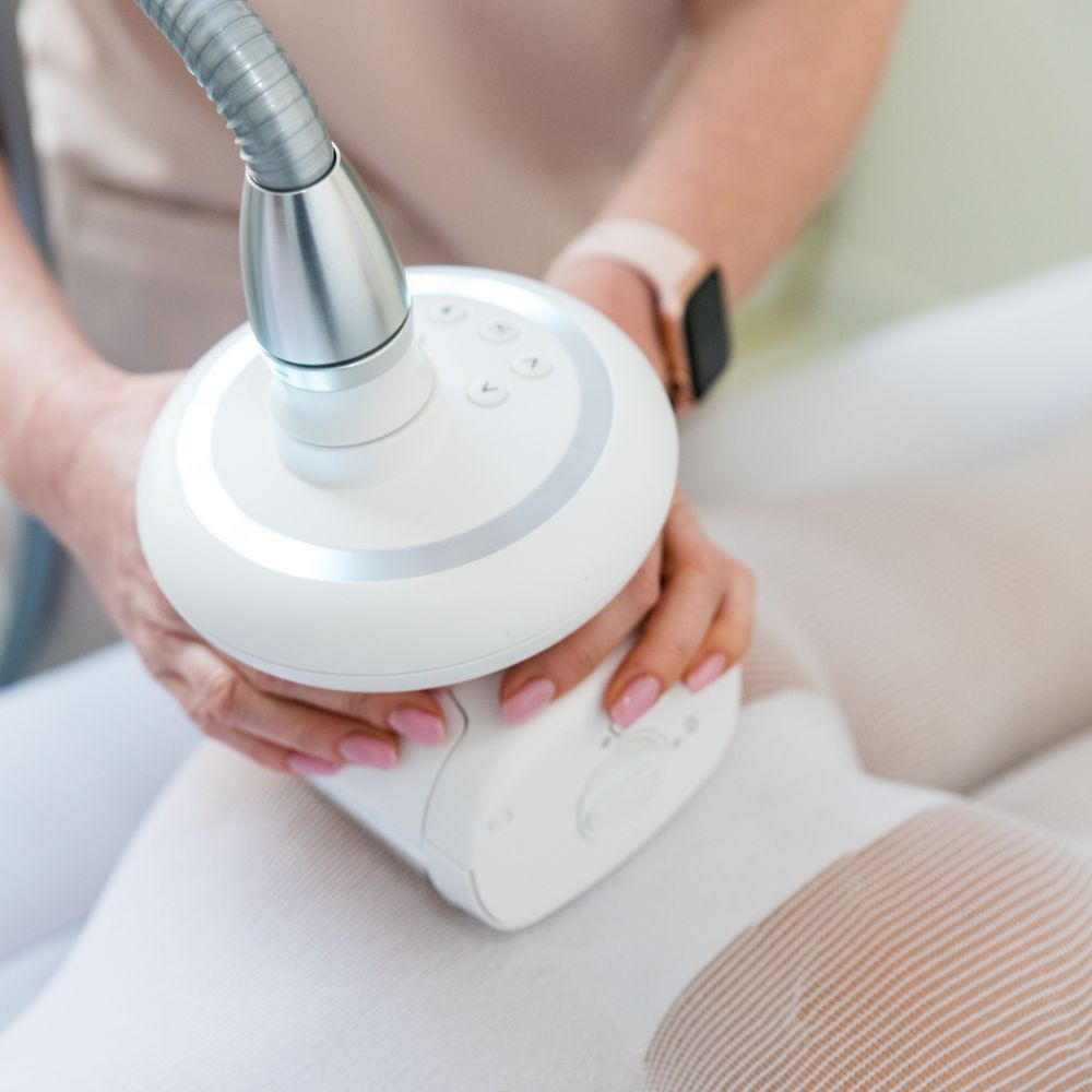 Zabieg modelujący ciało przy użyciu specjalistycznego urządzenia, wykonywany na nogach klientki w gabinecie kosmetologii holistycznej.