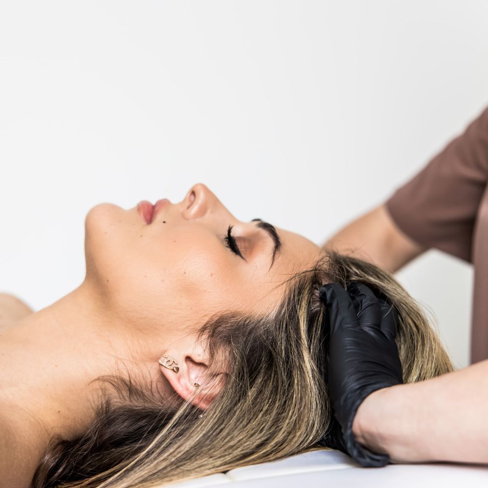 Relaksujący masaż skóry głowy wykonywany przez specjalistkę, klientka odpoczywa podczas holistycznej terapii